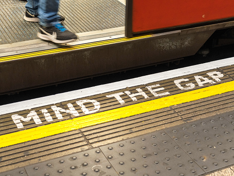 London, UK - A 'Mind The Gap' warning on the London Underground station platform, as a disembarking passenger prepares to step down from the subway train onto the platform.