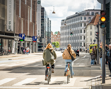 Copenhagen, Denmark - A rear view of two cyclists in afternoon sunshine, passing a pedestrian crossing in downtown Copenhagen.