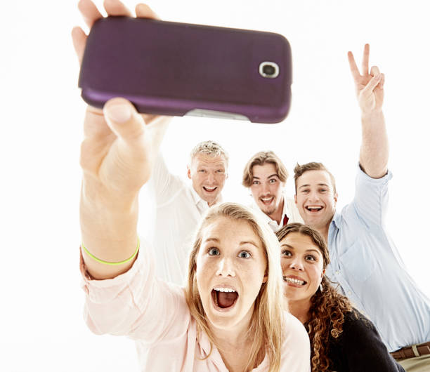 pięciu szczęśliwych mężczyzn i kobiet uśmiecha się, śmieje i gestykuluje, gdy trzyma się telefon komórkowy, aby zrobić selfie - human hand holding iphone iphone 5 zdjęcia i obrazy z banku zdjęć