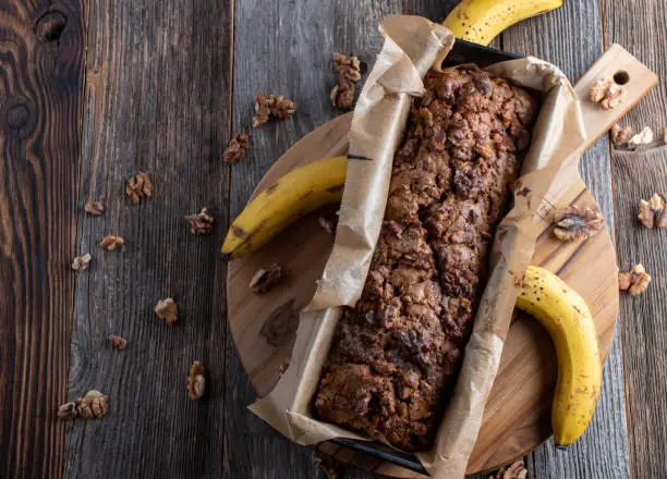 Delicious homemade banana bread or banana cake with caramelized walnut topping. Served isolated  in a loaf pan on rustic and wooden table background. Top view with copy space
