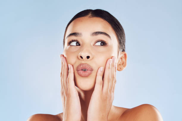 Closeup face beautiful young mixed race woman. Attractive female touching her face in studio isolated against a blue background. A skincare regime to keep your skin soft, smooth, glowing and healthy Closeup face beautiful young mixed race woman. Attractive female touching her face in studio isolated against a blue background. A skincare regime to keep your skin soft, smooth, glowing and healthy puckering stock pictures, royalty-free photos & images