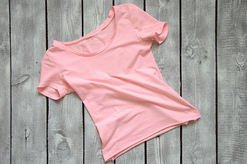 pink women's t-shirt lies on a white wooden table, t-shirt on a wooden background