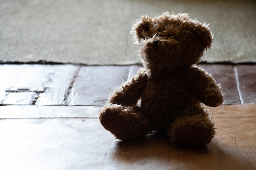 brown teddy bear sits on an old wooden floor in a dark room, childrens toy on the floor, fear