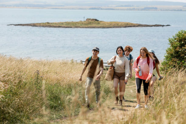 Hiking up the Coastline Wide angle shot of a group of mixed ethnic teens on a walk along the coastline together at Holy Island in the North East of England in summer. eco tourism stock pictures, royalty-free photos & images