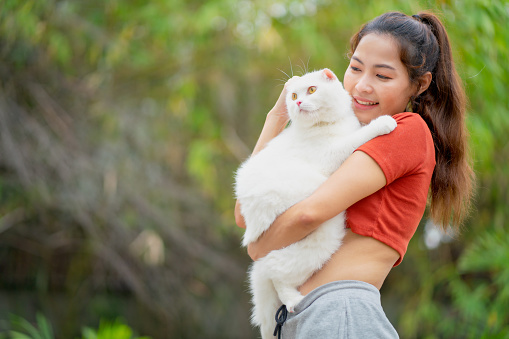 Asian pretty woman hold and hug white cat with happiness in garden with day light.