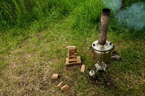 Boiling samovar in the forest with fire wood and tea glasses