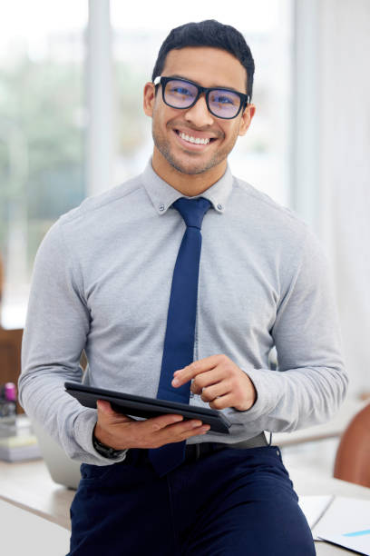 istock Young mixed race businessman holding and using a digital tablet standing in an office at work. One content hispanic male businessperson typing on a digital tablet at work 1398844451