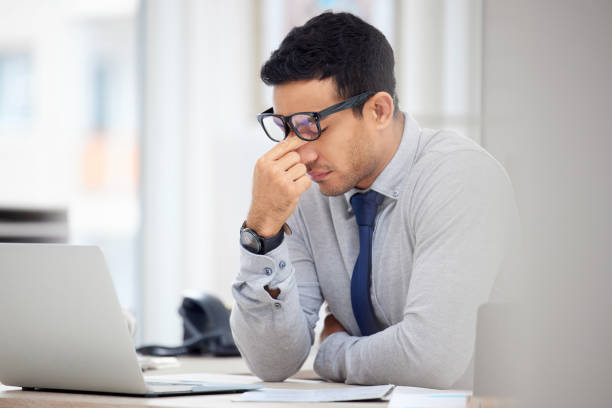 istock Tired mixed race businessman suffering from a headache while working on a laptop at work. Stressed hispanic male businessperson looking upset in an office 1398844471