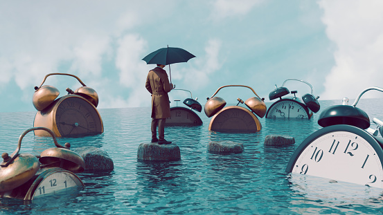 Concept of dealing with issues related to time. Man stands with umbrella outside looking at large collection of big alarm clocks drowning in the sea.