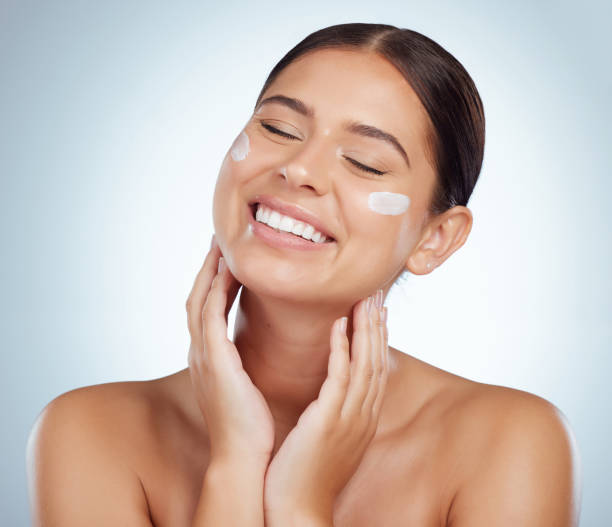 istock Smiling beautiful woman applying face cream while posing with copyspace. Caucasian model isolated against grey studio background with product on cheek. Moisturise and sunscreen for healthy skincare 1398845793