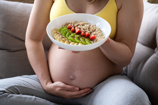 Belly of pregnant woman and plate with oatmeal and fruits. Nutrition and healthy diet during pregnancy. Healthy breakfast full of vitamins for pregnant woman.
