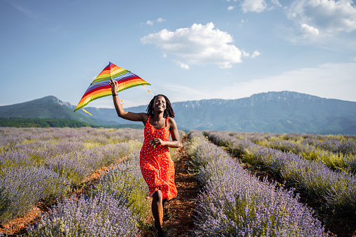 Happy black woman walking through lavender field with a kite