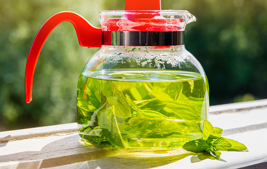 Close up view of fresh leaf peppermint tea in glass transparent tea jug on sunny summer morning. Homemade peppermint tea concept.