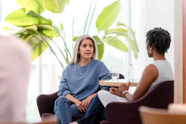 serious mature woman listens to unrecognizable female therapist - concentration multi ethnic group meeting business imagens e fotografias de stock