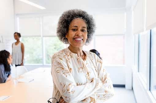 The successful, confident female senior adult CEO smiles for the camera after a meeting with her employees.