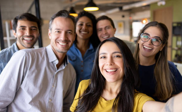 szczęśliwa grupa współpracowników robiących selfie w biurze - multi ethnic group business meeting 20s 30s zdjęcia i obrazy z banku zdjęć