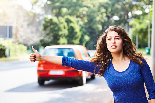 istock Beautiful young woman hitchhiking on the roadside on a road heading into the country 1398856821