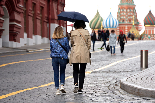 Moscow, Russia - May 2022: Two women walking with one umbrella on background of St. Basil's Cathedral on Red square