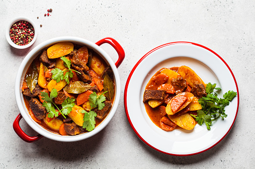 Beef stew with potatoes, carrots in tomato sauce in red pot, gray background, top view.