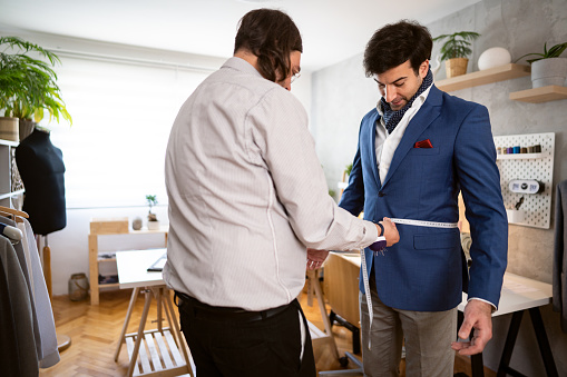 At the design studio, Caucasian male fashion designer and tailor, measuring the male client, during suit rehearsal