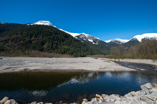 View of snow-capped mountains reflecting in the Squamish river in British Columbia, Canada, on a bright sunny day in Springtime.