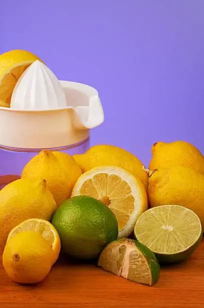 A colorful display of Lemons and limes, in front of a juicer, some cut and some whole.