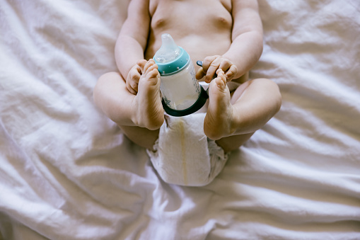 A Caucasian 7 month old boy holds a bottle of milk based baby formula.  A shortage in formula in the United States is affecting food security for many families.