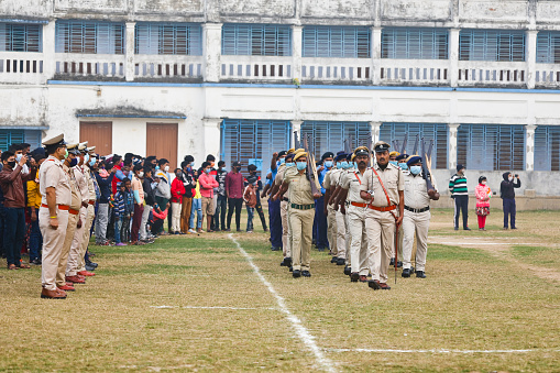 Katwa WB India - January 26, 2022 : Taken this picture in the town of Katwa in state of West Bengal on Republic Day Morning. In the picture police saluting to District Magistrate who hoisted the Indian Flag on school ground. In background are spectators witnessing the flag hoisting sitting on the top of the school building.