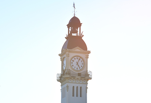 Clock tower building. Large clock tower with hour hands that shows the time of day and night. Clock tower on blue sky.  Telling time on Clock tower. Clocks with time on building.