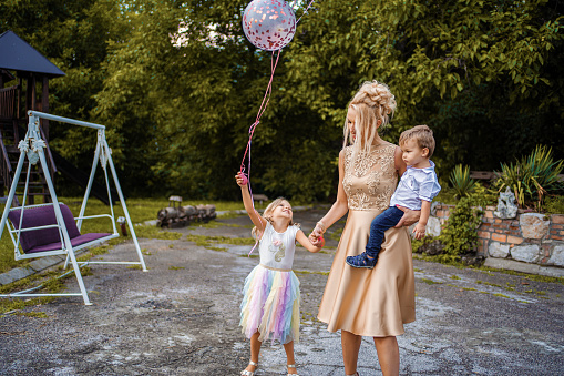 Elegant mother with her two cheerful kids walking with balloons