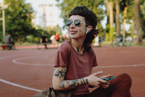Portrait of millennial woman with tattoos. Woman who looks like non-binary or retro styled using smart phone stock photo