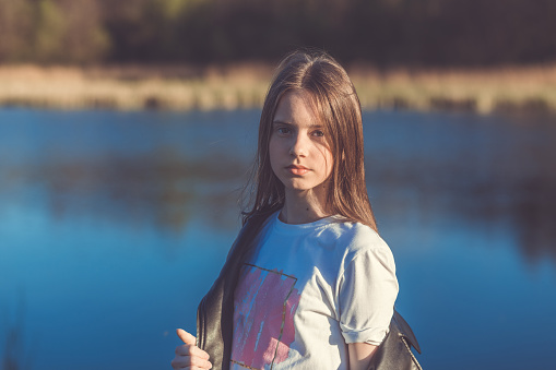 Portrait of a beautiful happy teenage girl outdoors in spring. A girl poses on lakes shore.