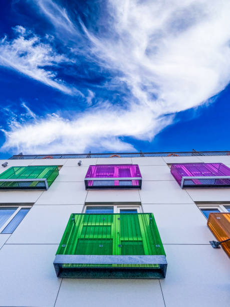 Colorful little deck or patio spaces in green, orange and magenta set against an otherwise plain-looking residential building. A bright blue sunny sky hangs above the scene.