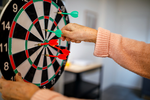 The senior woman plays darts at home and has a good time