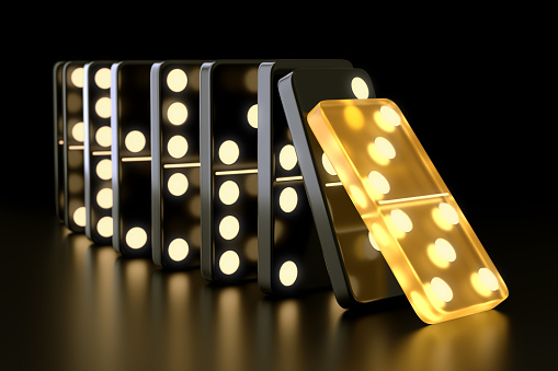 Unique glowing yellow domino tile falling on black dominoes on dark background. Leadership, teamwork and business strategy concept. 3D illustration