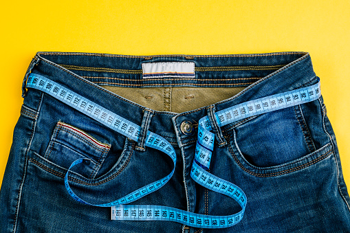 The concept of a healthy lifestyle and diet. Blue jeans with a blue measuring tape instead of a belt.