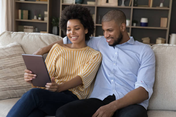 istock Beautiful African couple relaxing on sofa using digital tablet 1398880160