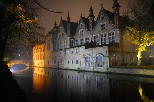 Typical Bruges houses illuminated and reflected in the canal at night in winter.