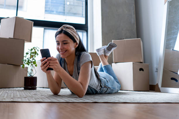 istock Beautiful young woman taking a break from packing boxes lying on front on the floor while looking at social media on smartphone smiling 1398882506