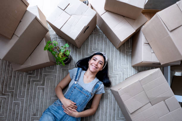 istock Beautiful young woman taking a break from unpacking boxes lying down on the floor facing camera smiling with a toothy smile 1398882518
