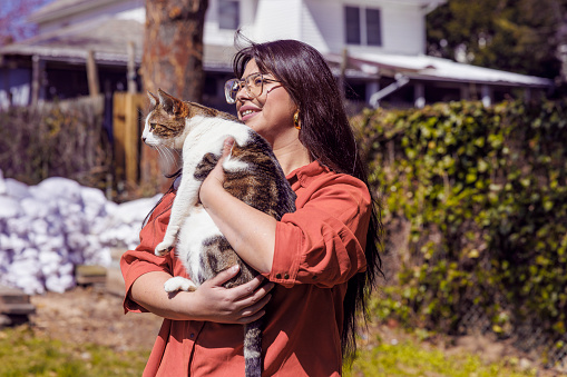 Young woman holding her cat when she is walking outdoor in a sunny day in spring.