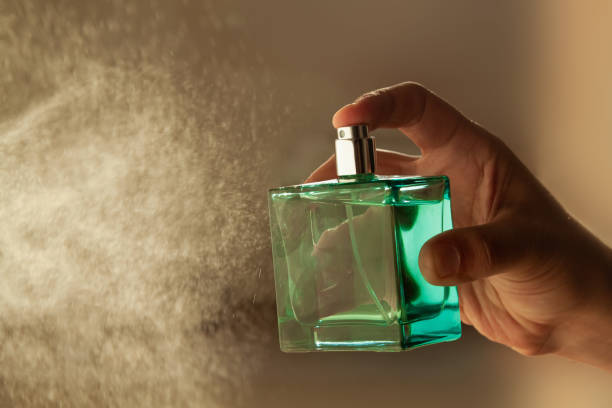 la mano del hombre rociando perfume de lujo sobre un fondo claro. - perfume bottle scented cosmetics fotografías e imágenes de stock
