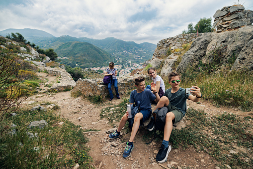 Mother and three teenage kids are hiking on a spring day in Sicily, Italy. They are sitting and resting on top the hill. \nCanon R5