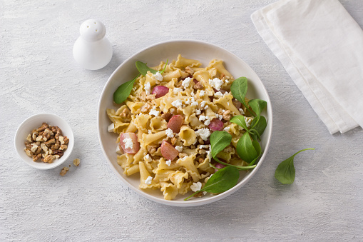 Italian pasta campanelle with radishes, feta cheese, walnuts and arugula in a white plate on a light gray background, top view. Delicious homemade food