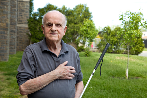 Blind senior man outdoors, hand on heart.