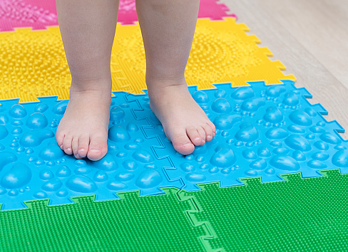 People. Children's small legs stand on multi-colored massage rugs. Health concept. Soft focus. Close-up