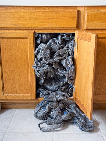 Oversupply of plastic shopping bags, a cabinet overflowing with plastic waste that could be recycled. We all have a supply of bags that can be reused, but at some point they should be taken in to be recycled. Gray plastic with oak finished cabinet with room for copy. A home lifestyle concern.