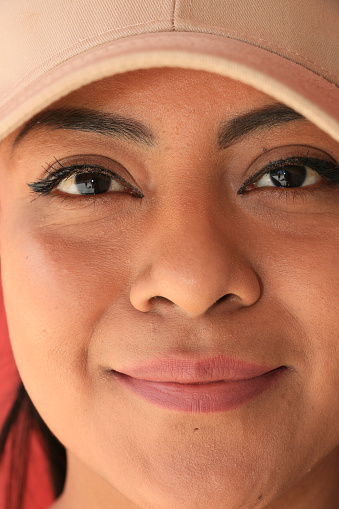 A closeup image of a Mexican woman's head. She is wearing a beige baseball cap.