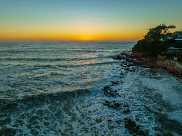 Clear skies aerial sunrise seascape Sunrise seascape with surfers and rocks at Avoca Beach on the Central Coast, NSW, Australia. avoca beach photos stock pictures, royalty-free photos & images