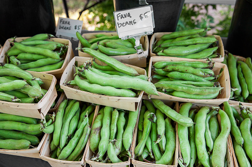 Fresh fava beans arranged in small wooden cartons for sale at a farmer's market.